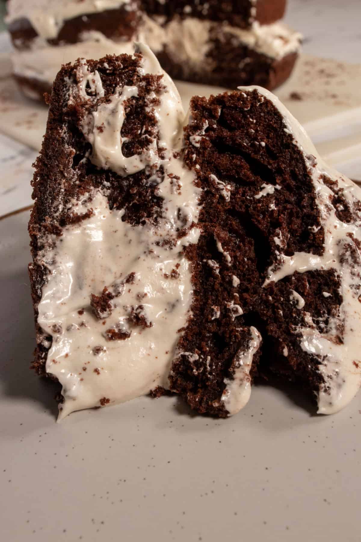 A smaller slice of vegan tiramisu cake on a serving plate. The chocolate cake looks moist from this angle. 