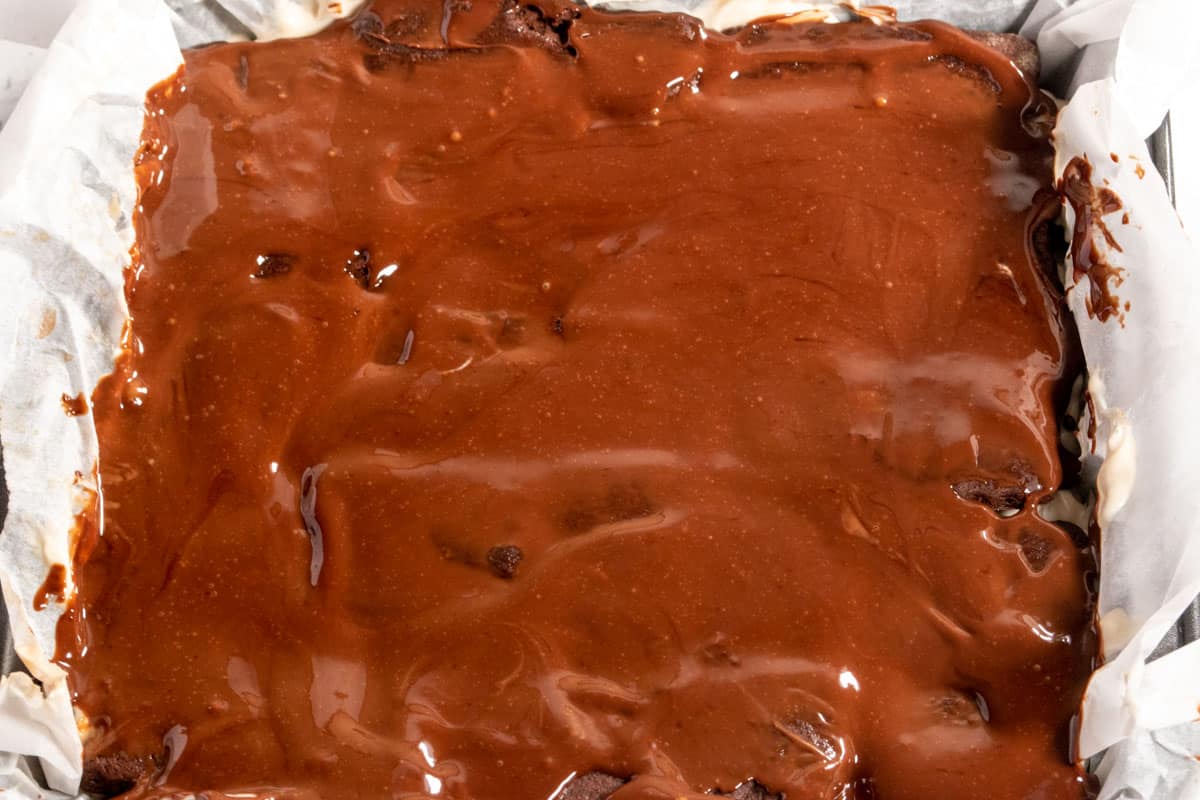 The chocolate topping has been poured over the over layers which have been created inside the lined square tin. It is ready to go in the fridge.