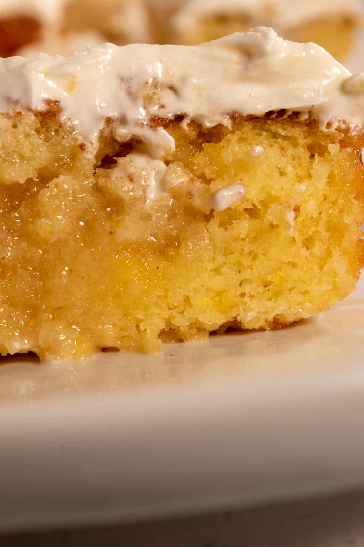 A large and moist slice of vegan lemon poke cake which is topped with a vegan cream cheese frosting. The filling is very visible and sits inside the center of the slice. 