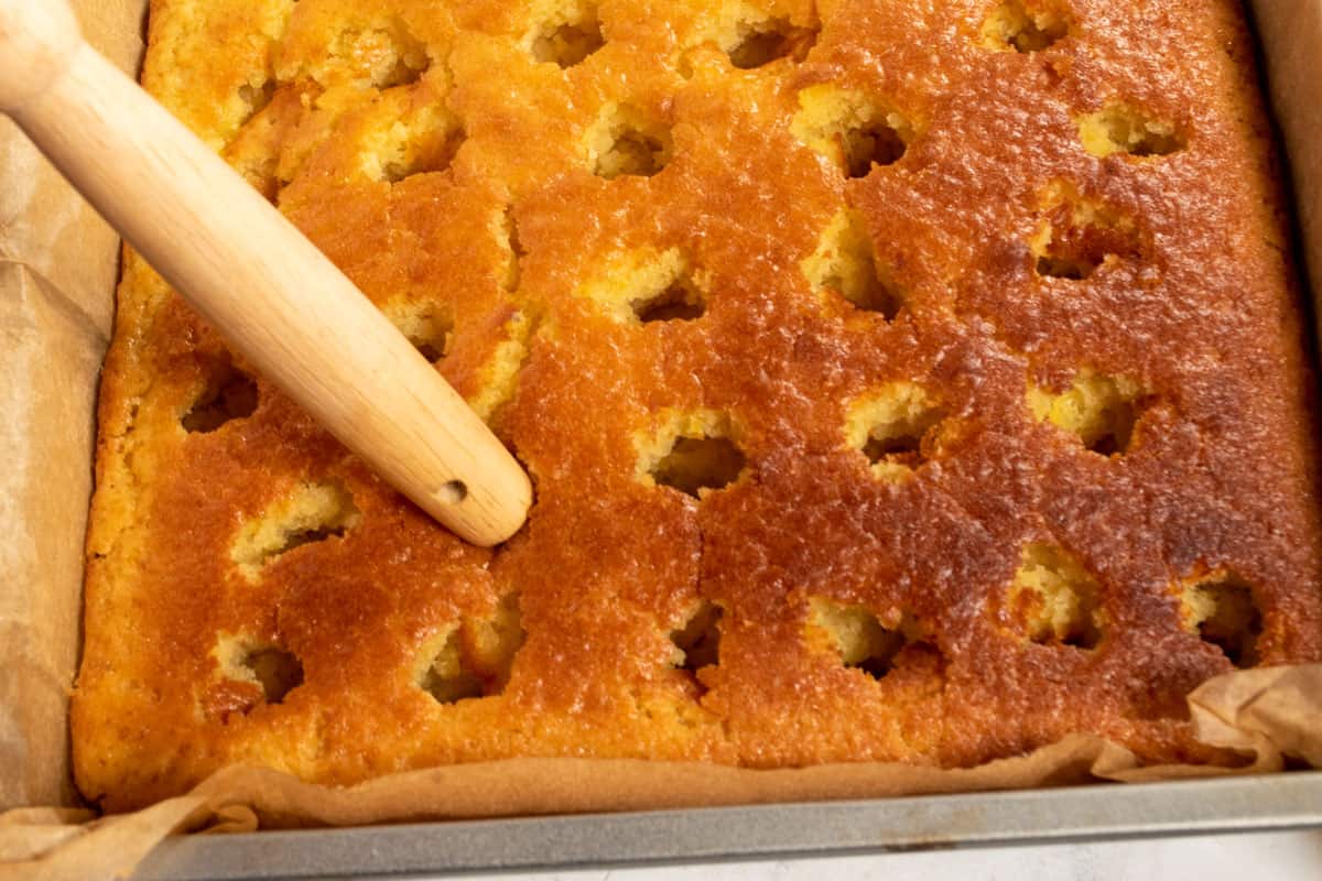 A large wooden spoon poking holes into the cake. 