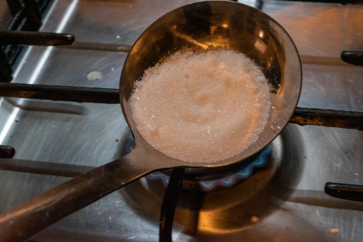 Sugar inside a large ladle being heated on a gas stove. 