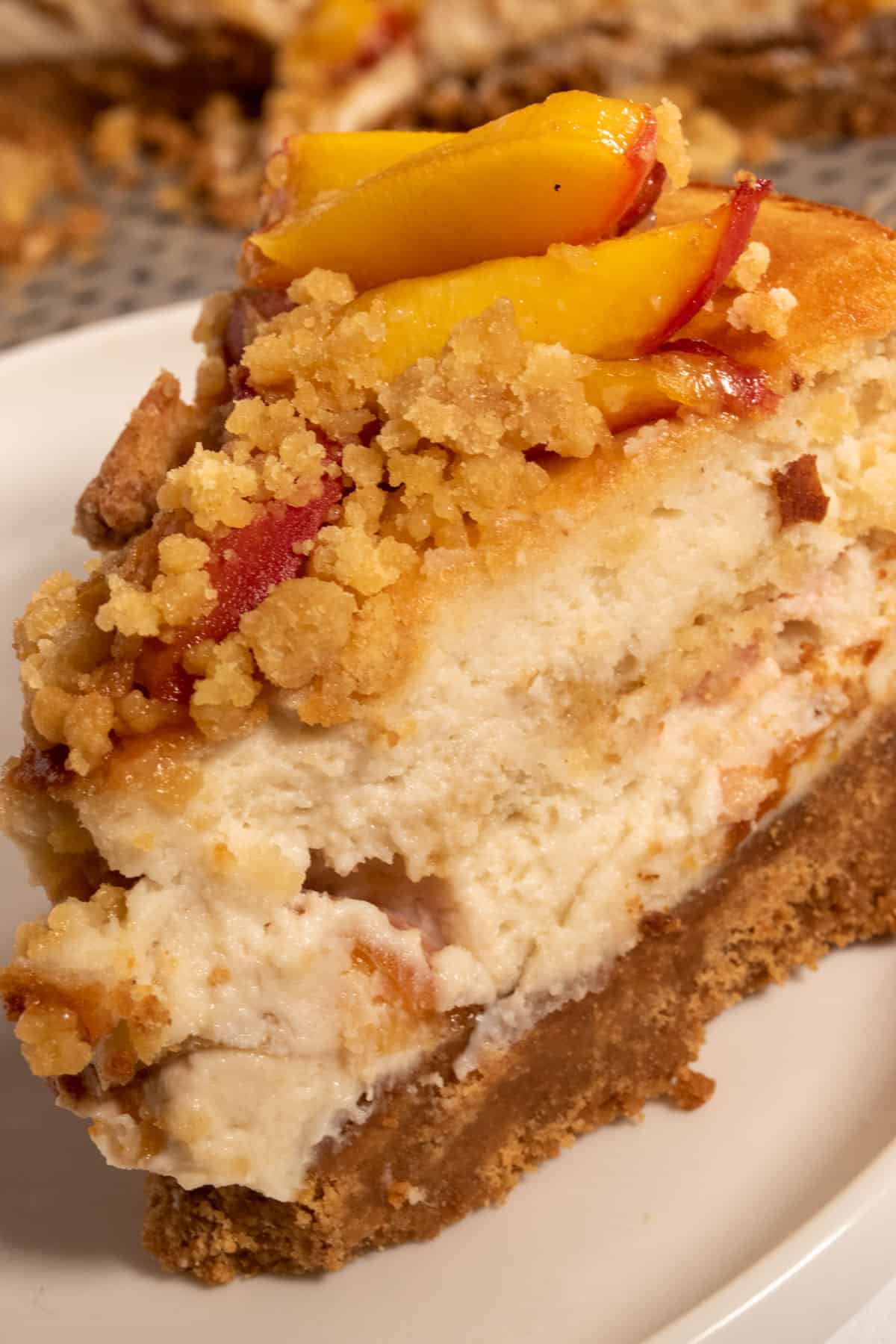A slice of vegan peach cobbler cheesecake looking creamy and golden in the lighting. 