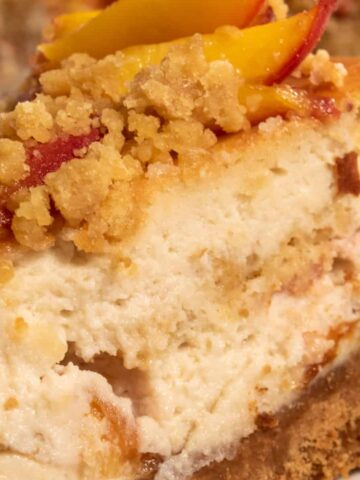 A thick, creamy slice of my vegan peach cobbler cheesecake, which is topped with streusel and fresh caramelised peaches.