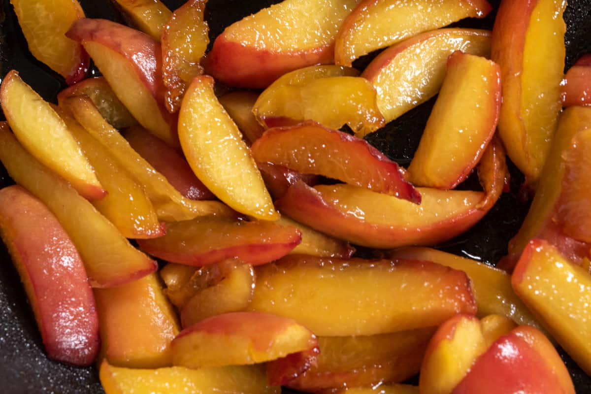The peaches being caramelised inside a large frying pan. They are golden. 