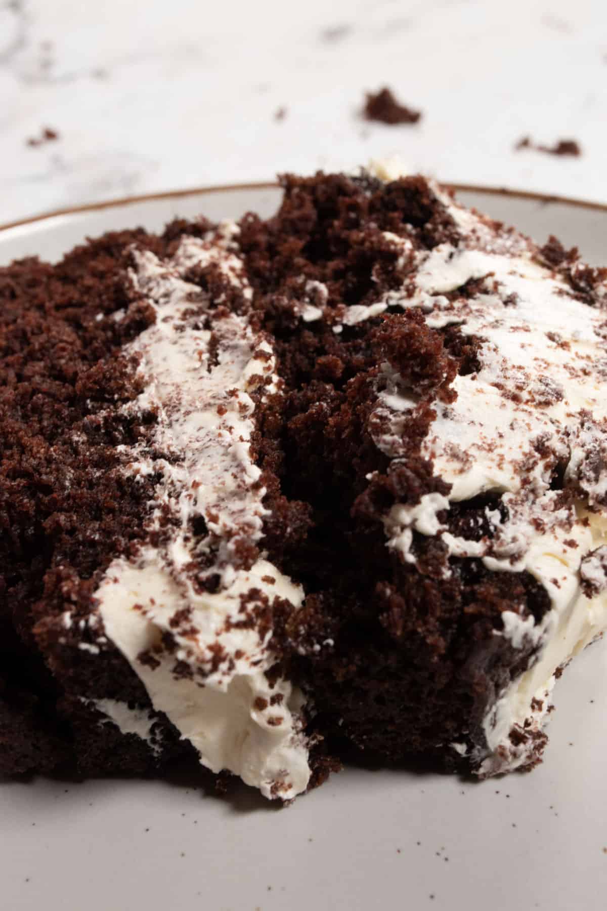 A very large creamy slice of vegan brownie cake sitting on a brown-rimmed white plate.