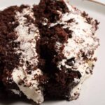 An incredibly thick slice of vegan brownie cake on a white plate, generously decorated with vanilla buttercream frosting.
