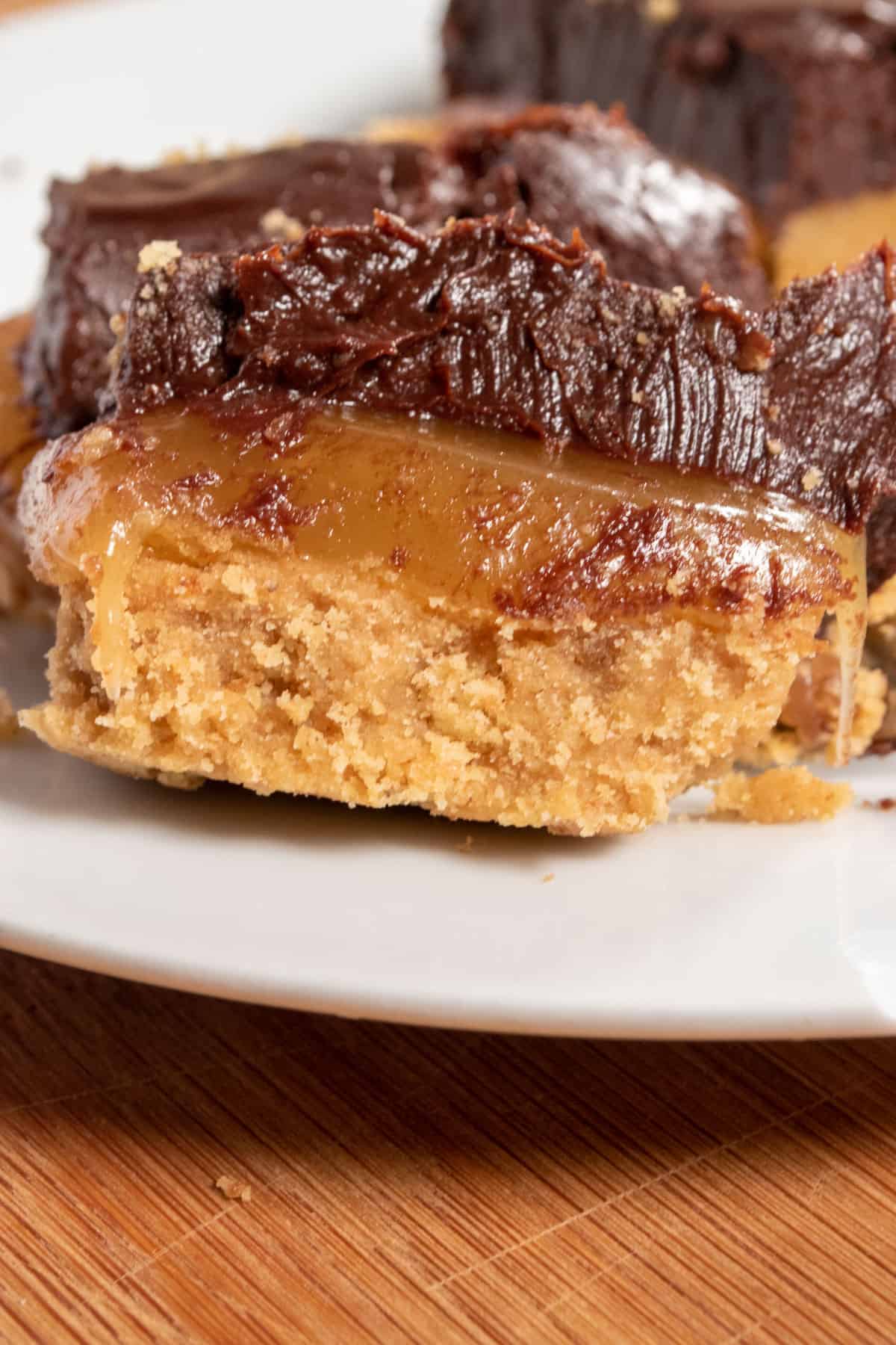 A chunky vegan caramel slice on a round, small white plate. Caramel is dripping from the center.