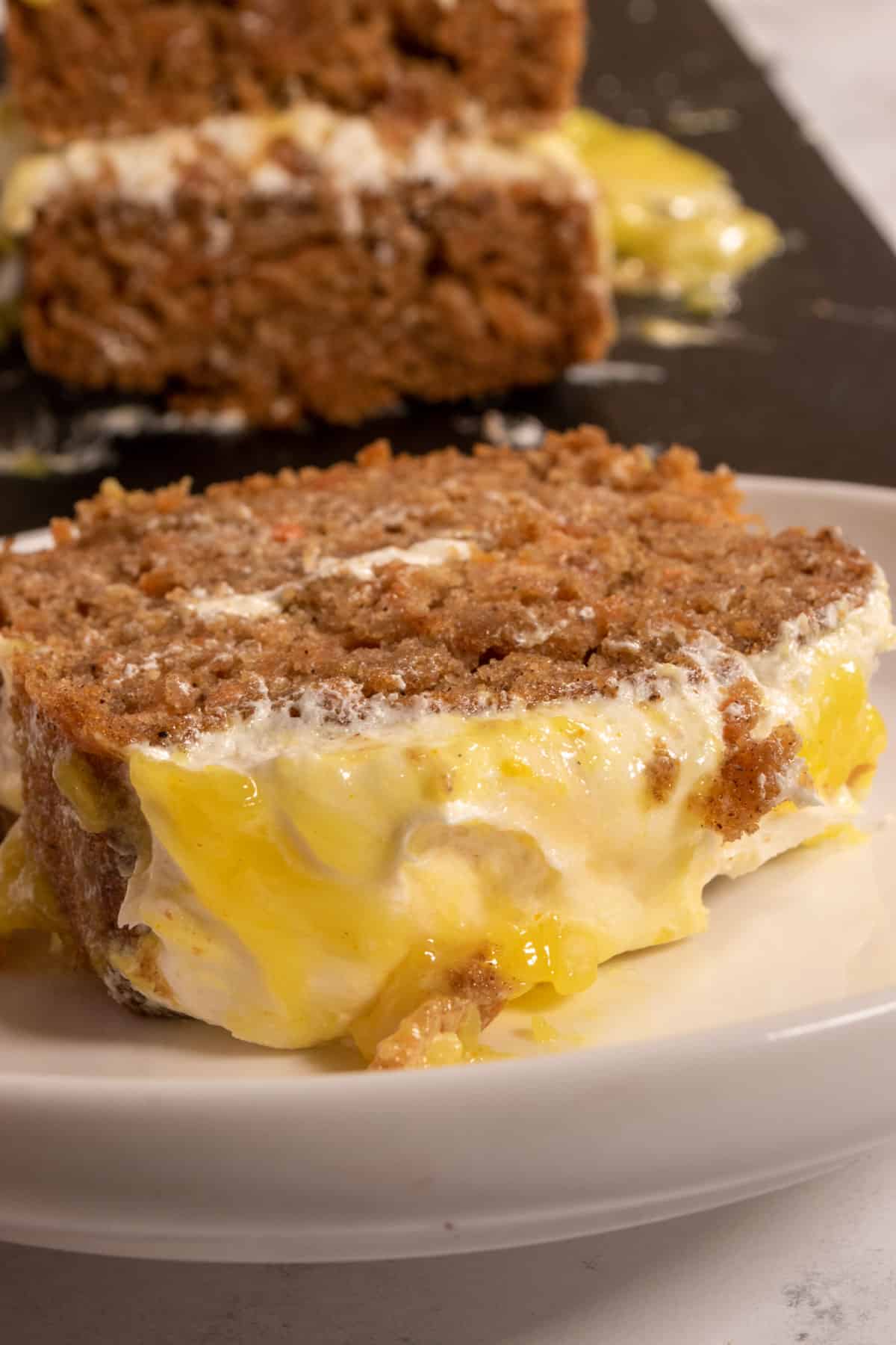 A thick slice of cake on a small, white plate. The curd on top is a bright yellow. 