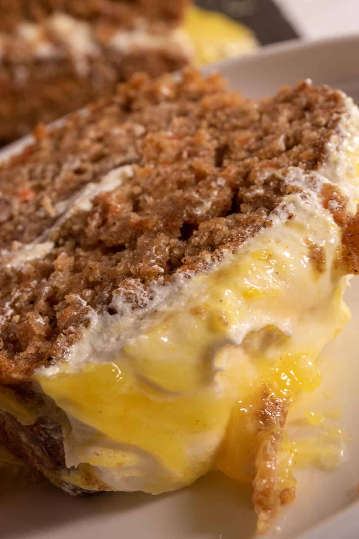 A slice of vegan carrot cake which is super soft, golden brown and topped with lemon curd. 