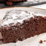 A chunky piece of vegan chocolate mud cake, topped with powdered sugar. It looks soft and fluffy.