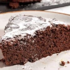A chunky piece of vegan chocolate mud cake, topped with powdered sugar. It looks soft and fluffy.