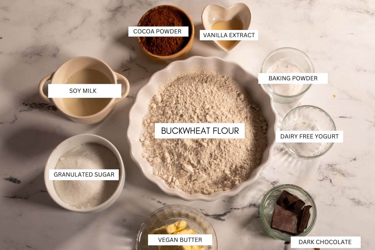 All the recipe ingredients that you will need to make my vegan chocolate mud cake. They are organized into a circular pattern on a white marble background. 
