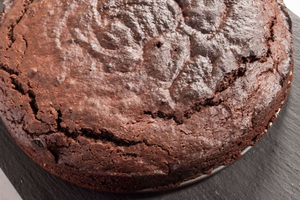 The baked vegan chocolate cake has been removed from the tin and is cooling down on a slate board. 