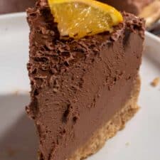 A thin slice of my vegan chocolate orange cheesecake being shown close up to the camera. It has a small slice of orange on top.