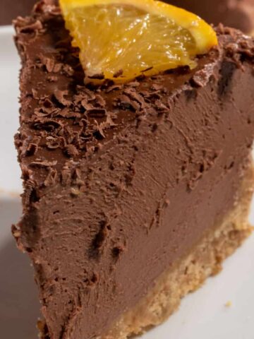 A thin slice of my vegan chocolate orange cheesecake being shown close up to the camera. It has a small slice of orange on top.