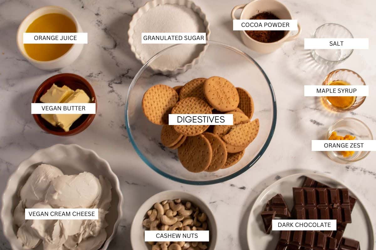 The eleven ingredients that you need to make a vegan chocolate orange cheesecake, laid out on a white marble background. 