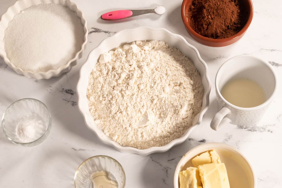 The ingredients that you will need to make vegan chocolate wafer cookies laid out neatly on a white, marble background. 