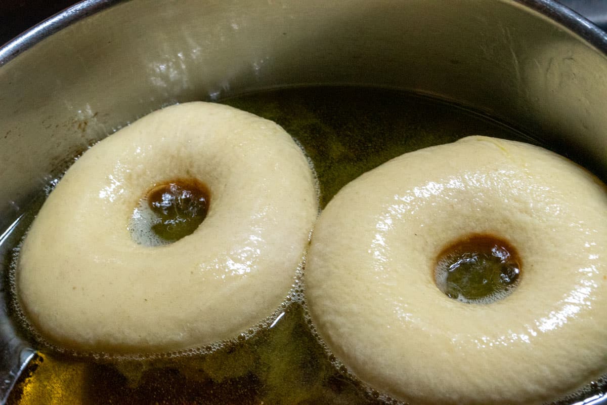 Two donuts frying inside a large saucepan. 