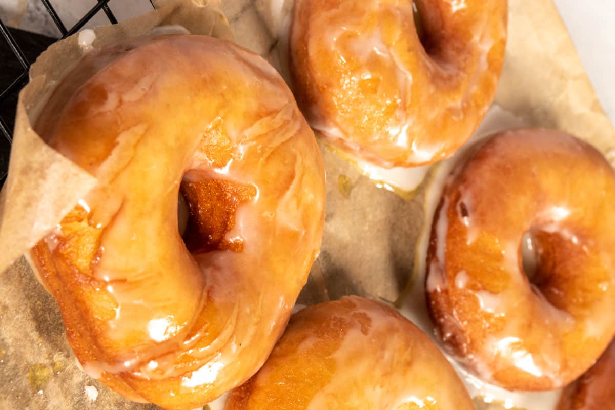 Four cooked, golden brown vegan krispy kreme donuts which are glazed and cooling down. 