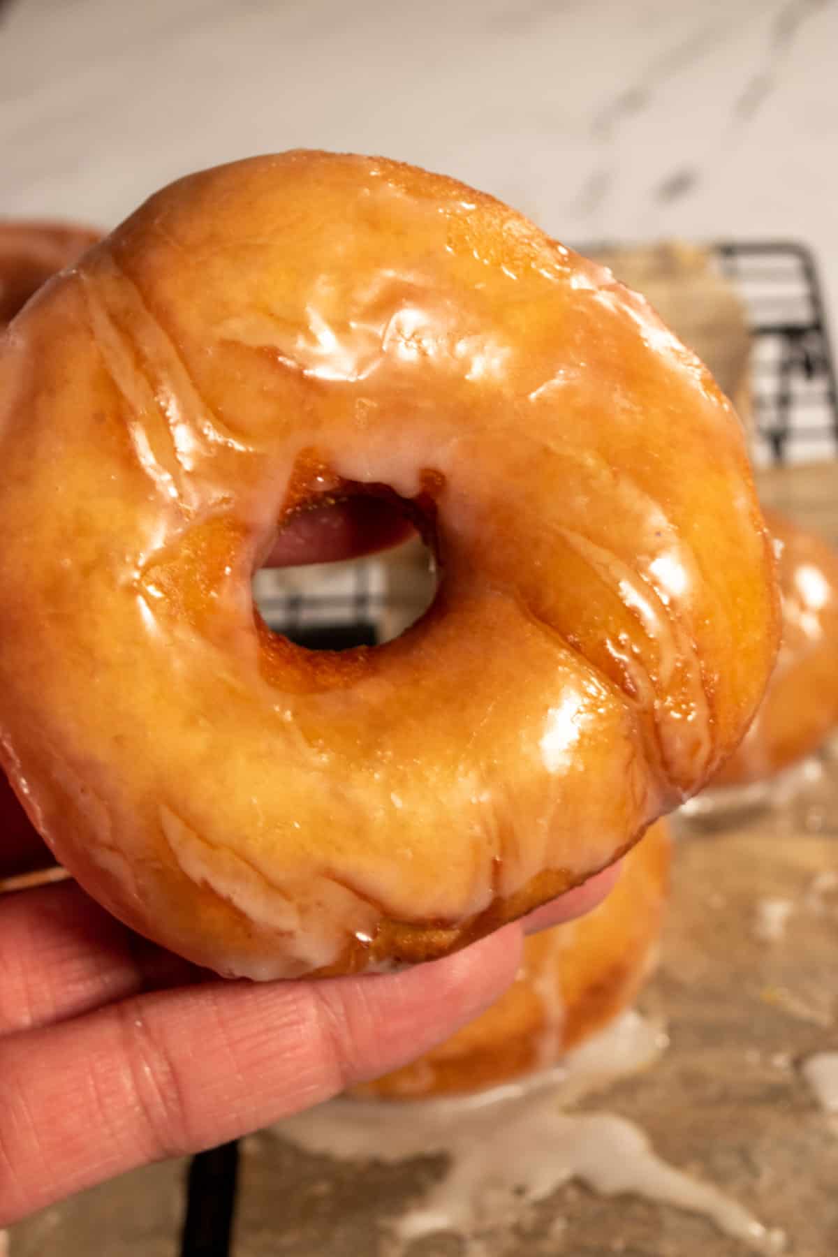 A single round donut being held in a hand. It is dripping with glaze.