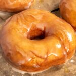 One of my vegan krispy kreme donuts on a sheet of parchment paper is glazed and looking soft and golden.