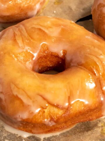 One of my vegan krispy kreme donuts on a sheet of parchment paper is glazed and looking soft and golden.