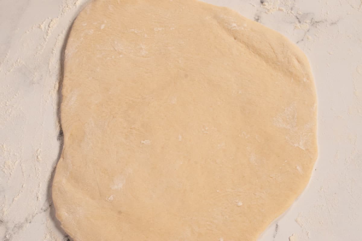 The risen dough, rolled out over a white, lightly floured background.