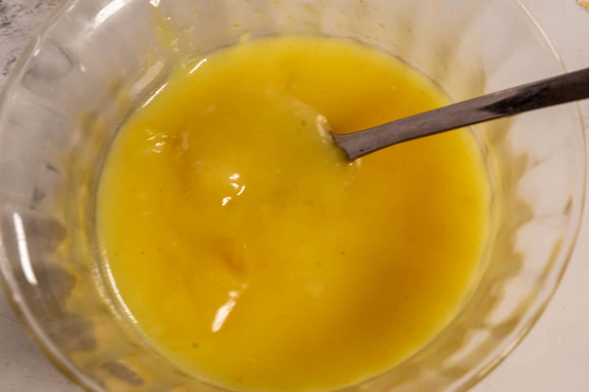 The lemon curd cooling at room temperature. It has thickened inside a small ramekin. 