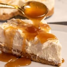A creamy slice of vegan caramel cheesecake with caramel being dripped onto it from a golden spoon.