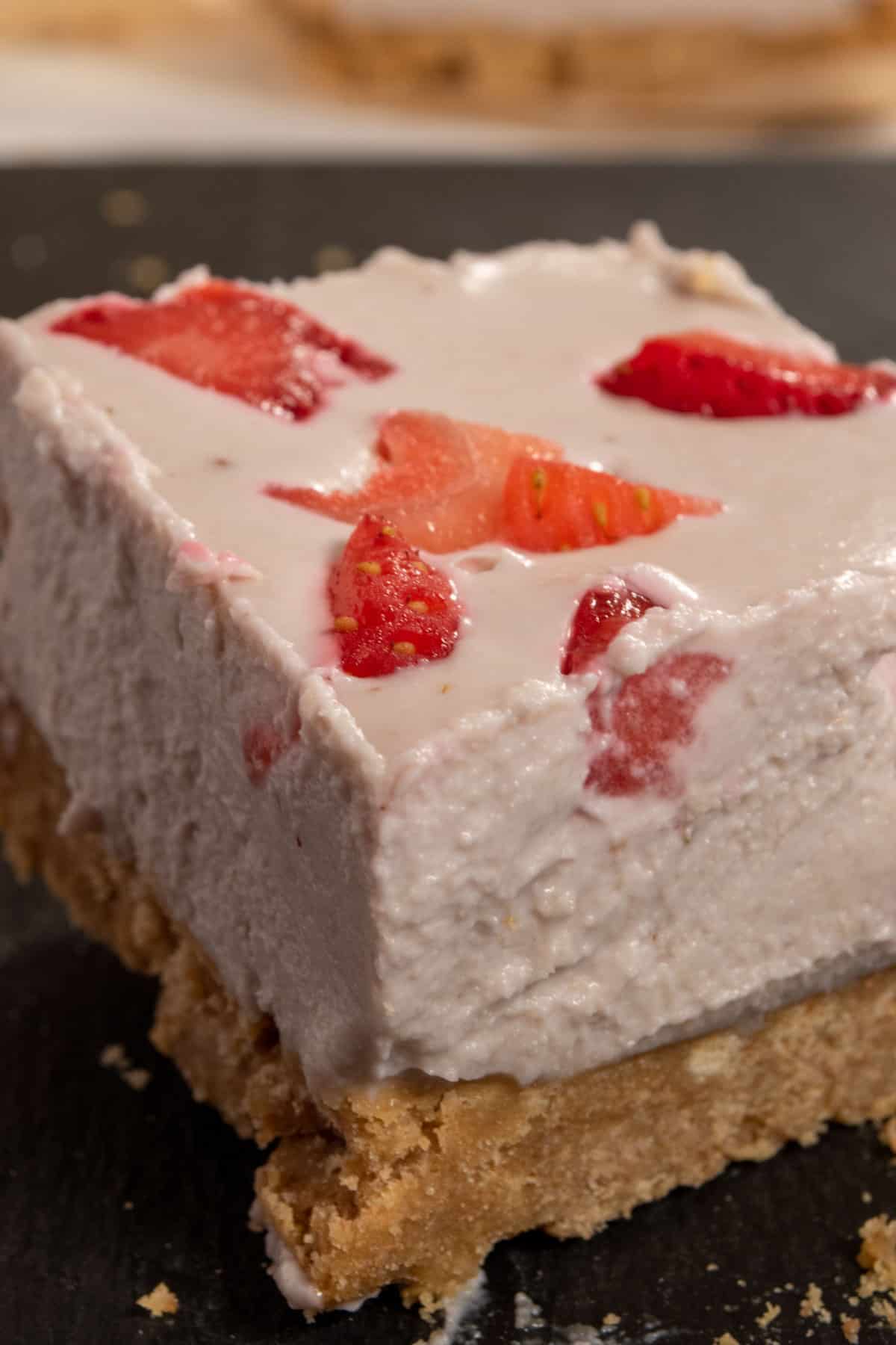 A silky smooth, cubic slice of my strawberry cheesecake which is perfectly pink, sitting on a black slate board.