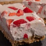 A very creamy vegan strawberry cheesecake bar on a slate chopping board topped with fresh strawberries.