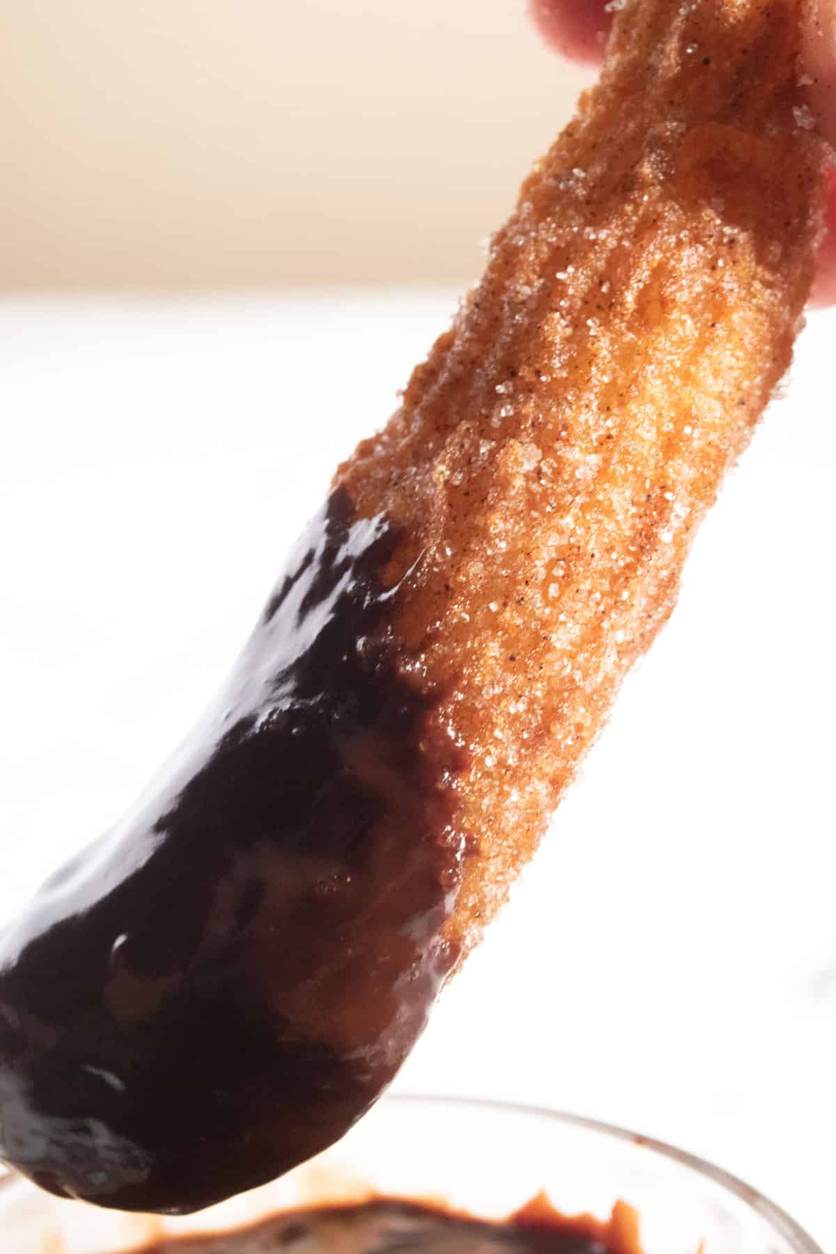 A large churro just after being dipped into vegan chocolate.