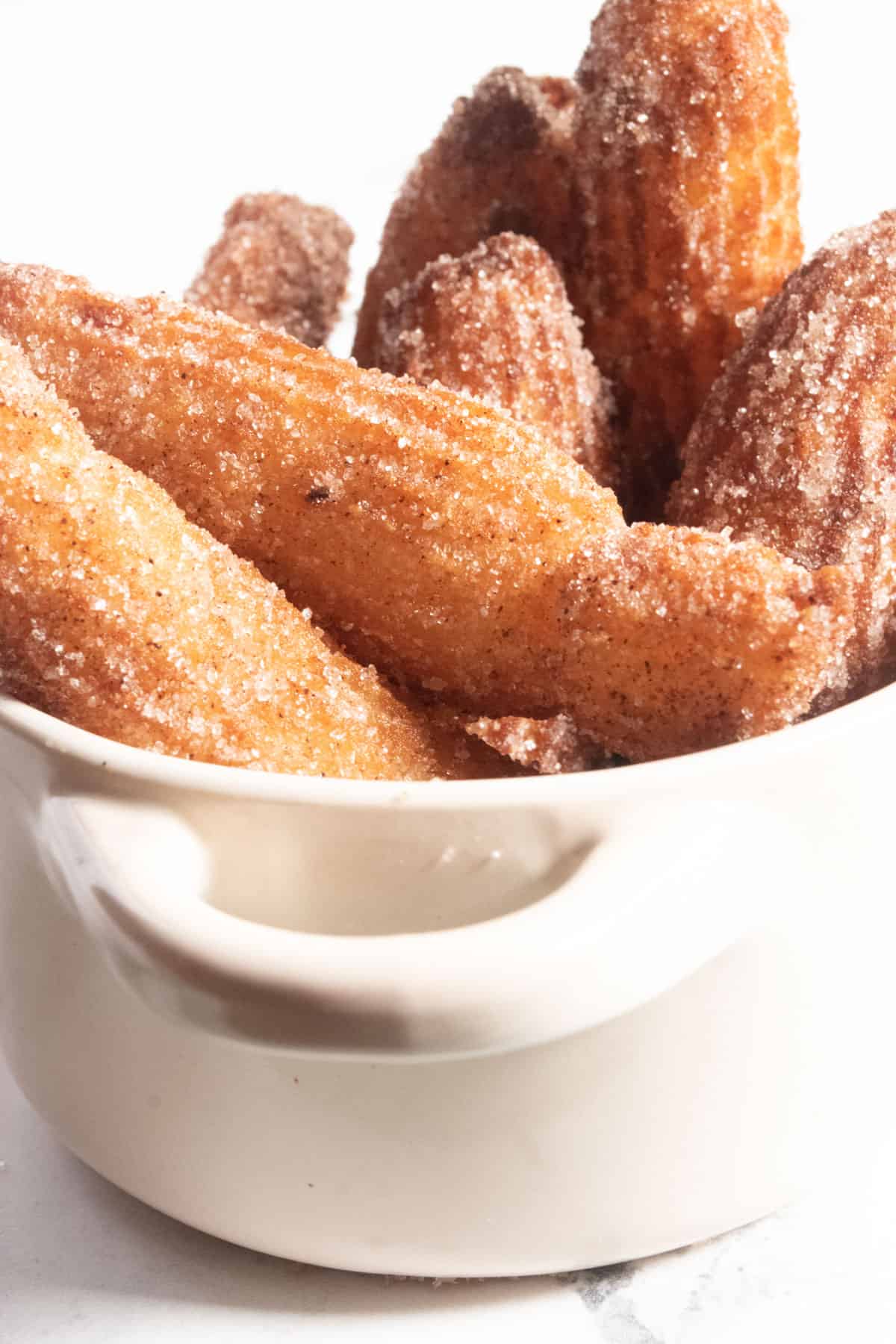 A close up shot of several vegan churros inside a small white pot. They are golden brown. 