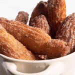 A pot full of vegan churros which are golden brown and coated with lots of cinnamon sugar.