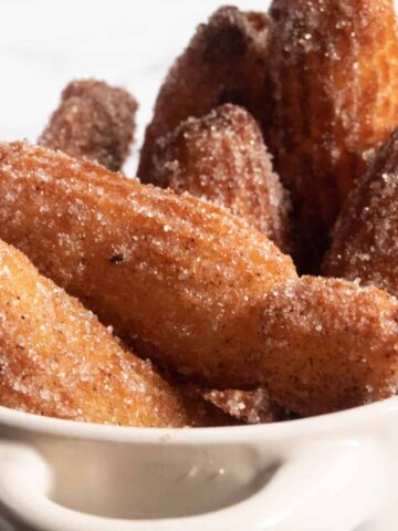 A pot full of vegan churros which are golden brown and coated with lots of cinnamon sugar.
