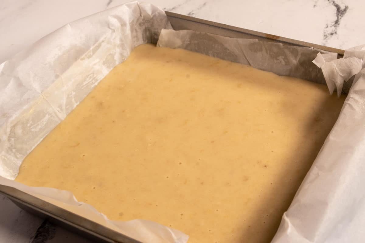 The cake batter has been poured into a square, lined cake tin. 