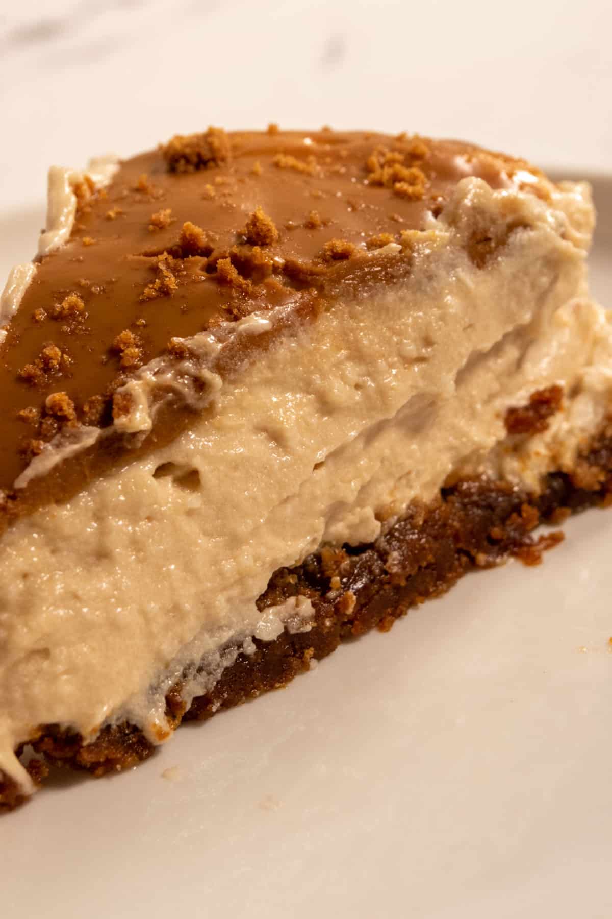 A regular-sized slice of vegan Biscoff cheesecake which is glowing in the light. The Biscoff layer on top is thick.