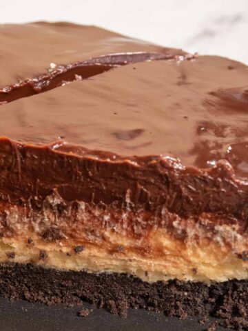 A whole vegan cookie dough tart sliced in half, revealing the inside layers. The chocolate on top is shiny.