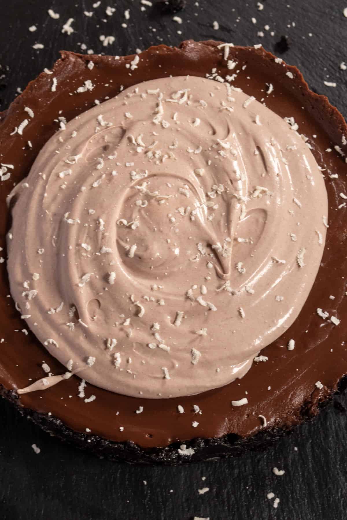 An overhead shot showing a whole vegan chocolate pudding pie which has a swirl of chocolate whipped cream on top and grated vegan white chocolate. 