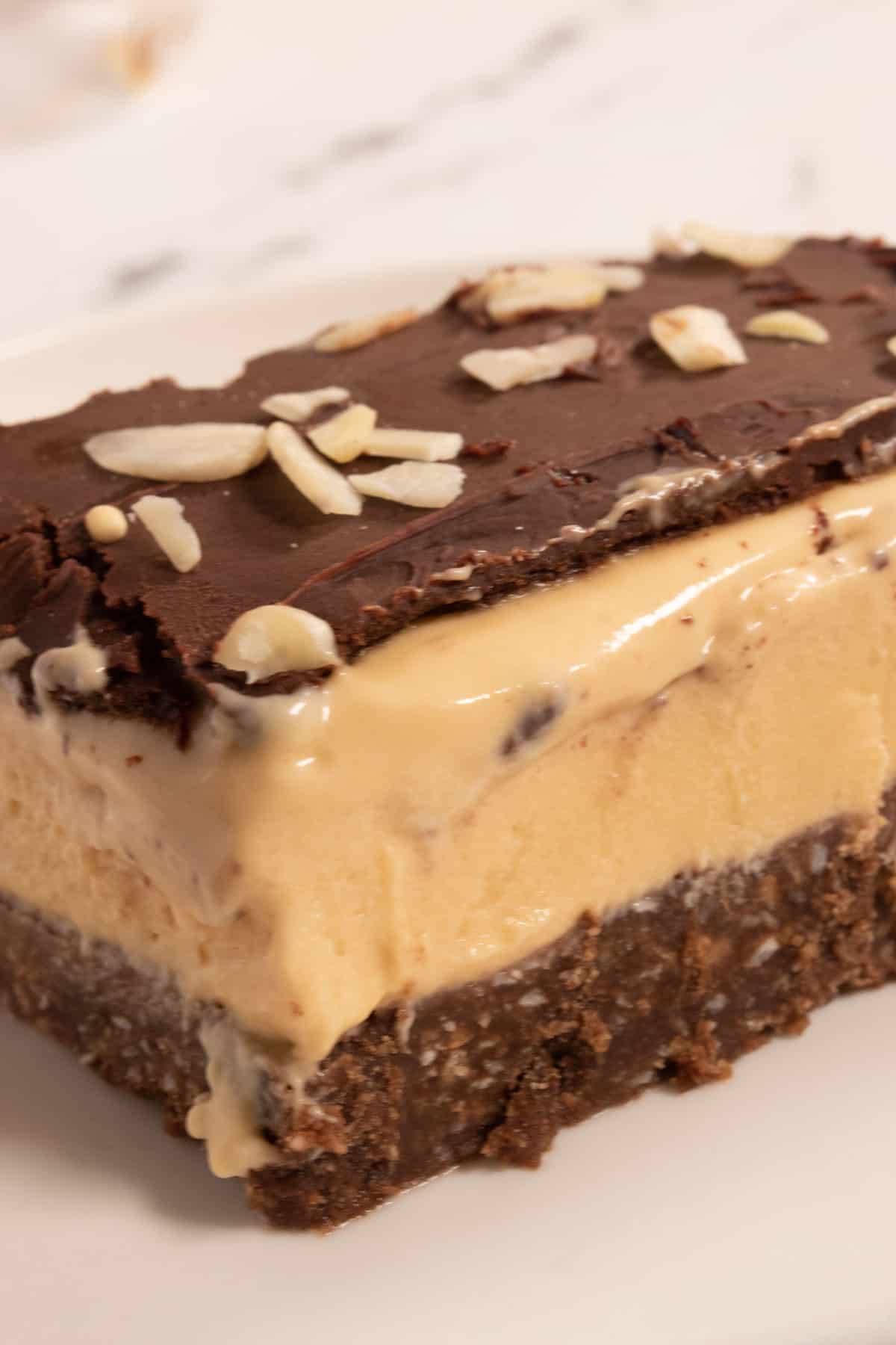 A large vegan nanaimo bar slice which a thick layer of custard in the centre on a white plate. 