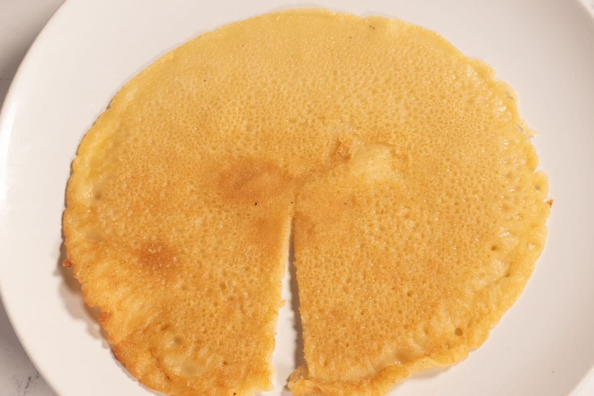 The fried crepe is on a white plate. A slit has been made from the rim to the center. 