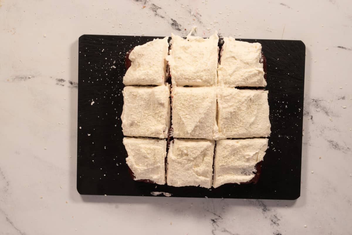 Vegan red velvet bars on a slate chopping board. They are topped with vegan white chocolate. 