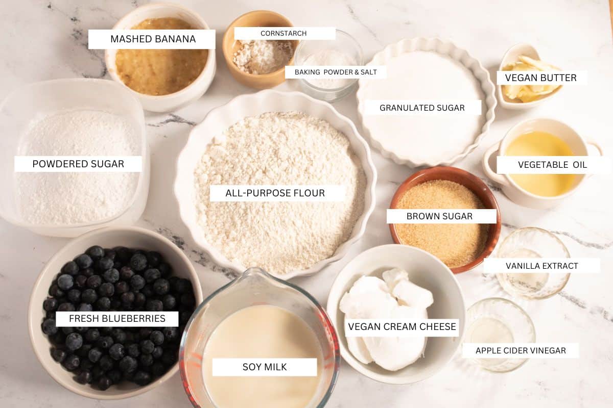 The ingredients that you will need in order to make my vegan blueberry cream cheese muffins all laid out on a white marble background. 