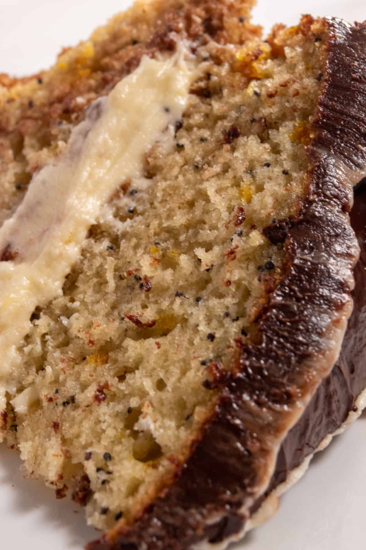 A chunky slice of vegan orange poppy seed cake which is topped with a thick ganache. Lots of buttercream frosting sits in the center of the cake. 