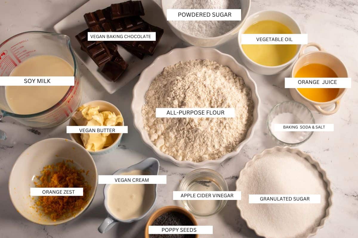 The recipe ingredients that you will need to make a vegan orange poppy seed cake laid out over a white marble background.