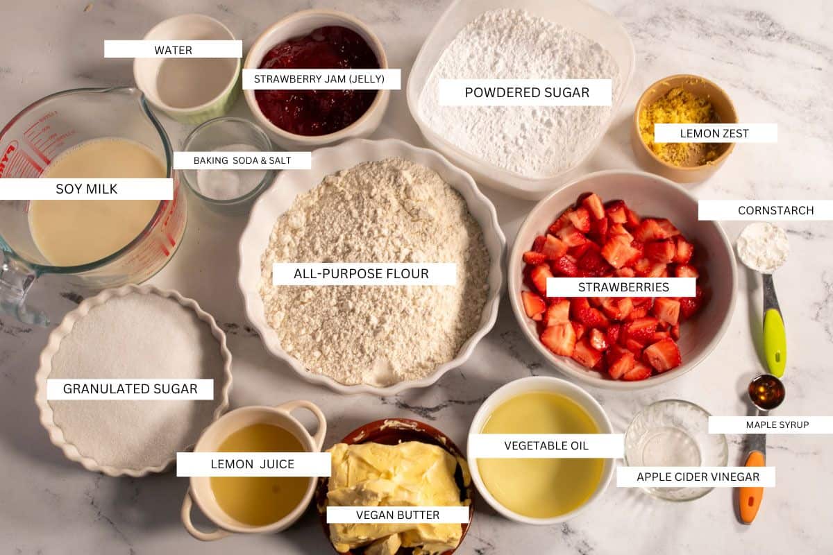 The ingredients needed to make vegan strawberry lemon cake laid out tidily on a white marble background. 