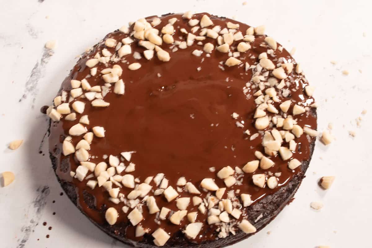The melted chocolate has been poured over the cake and chopped almonds have been sprinkled onto it. 