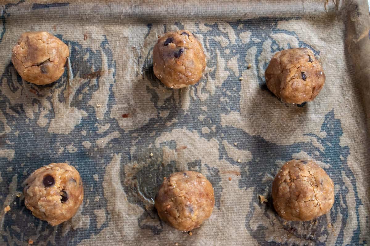 Six smaller cookies dough balls on a large baking tray. 