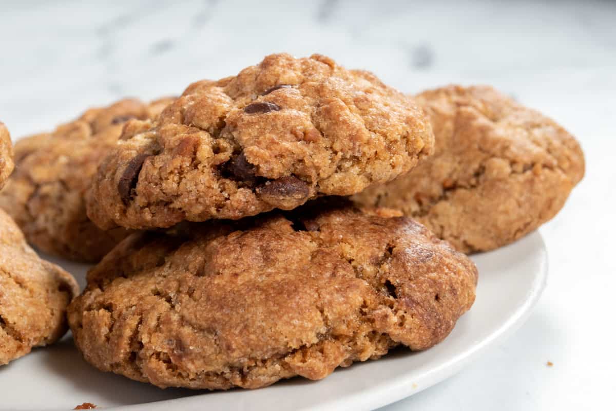 Several vegan Biscoff cookies piled onto a small, white saucer while they cool down. 