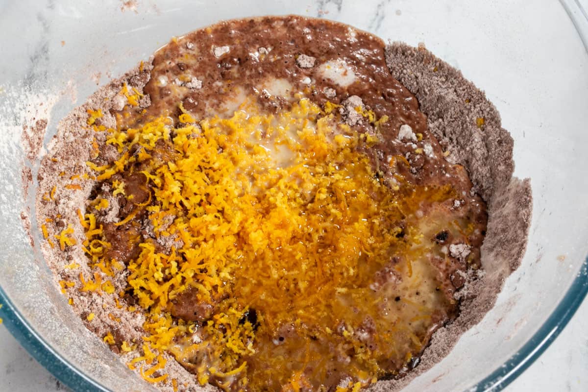 The wet ingredients including the vivid orange zest have been added to the bowl. 